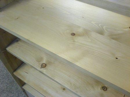 Surowe, jasne drewniane półki z widocznymi sękami, tworzące regał lub stand, sfotografowane pod kątem z góry.